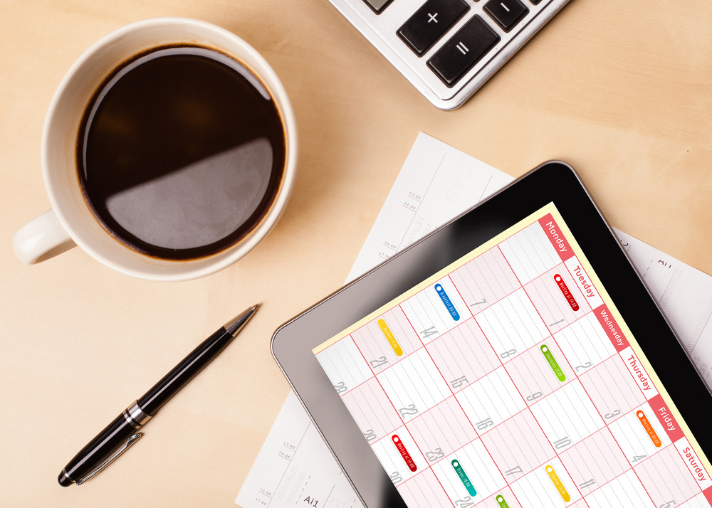 Workplace with tablet pc showing calendar and a cup of coffee on a wooden work table close-up Workplace with tablet pc showing calendar and a cup of coffee on a wooden work table close-up